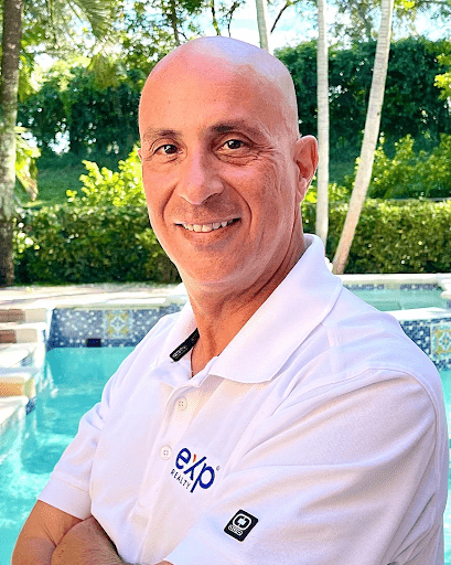 A bald man in a white shirt is standing in front of a pool.
