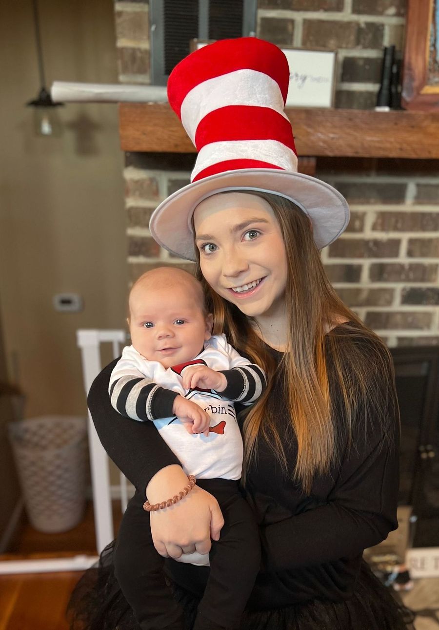 A woman wearing a cat in the hat is holding a baby.
