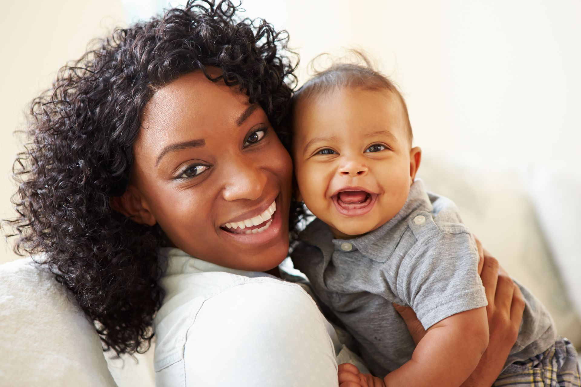 Woman holds a smiling baby; both are looking at the camera.
