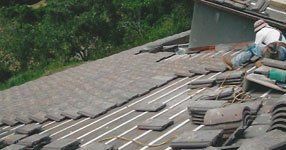 A man is laying tiles on the roof of a building.