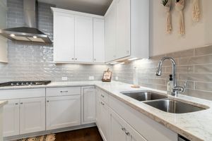 Bright white kitchen with marble counters, subway tile backsplash, stainless sink, and built-in range.