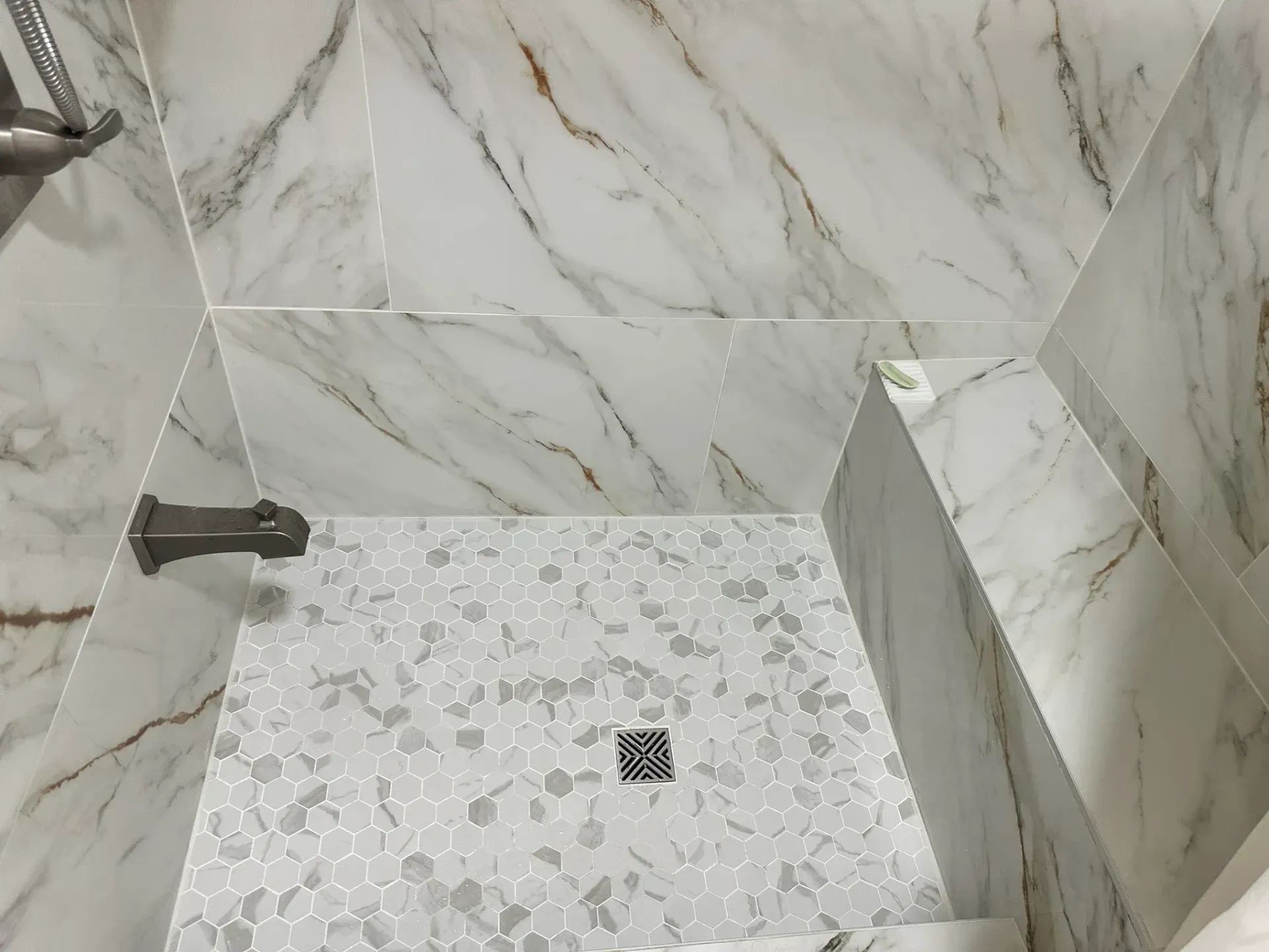 Marble-tiled shower with a square mosaic floor drain and wall-mounted fixtures