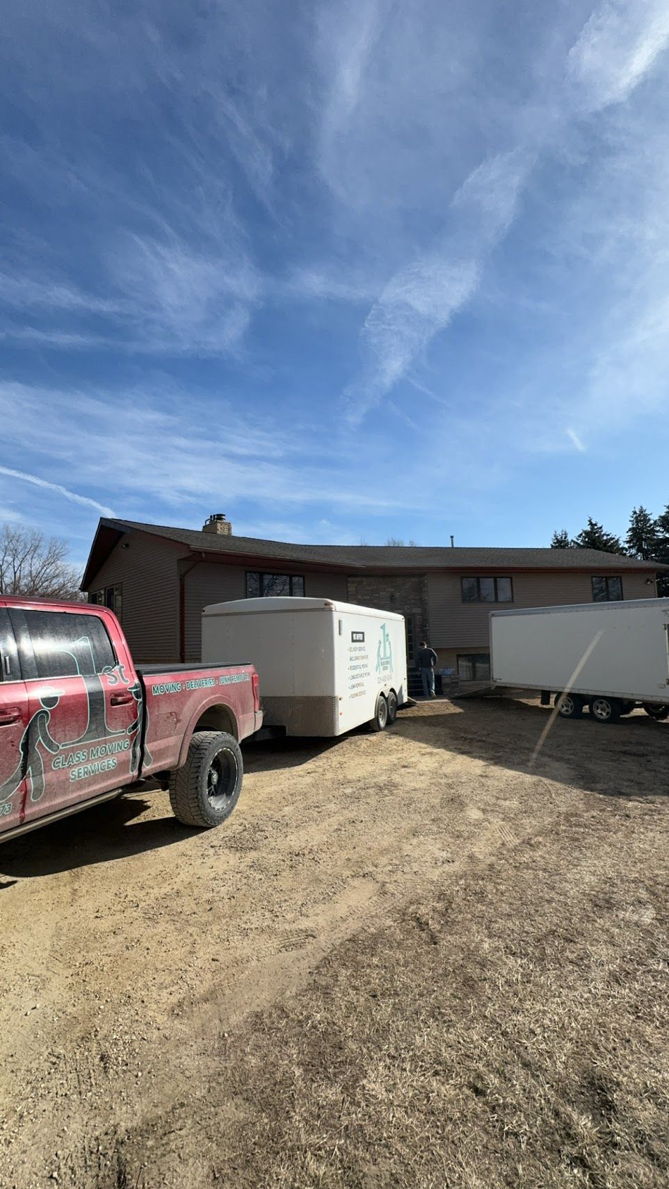 Red truck parked near a building with trailers in a dirt lot under a partly cloudy sky.