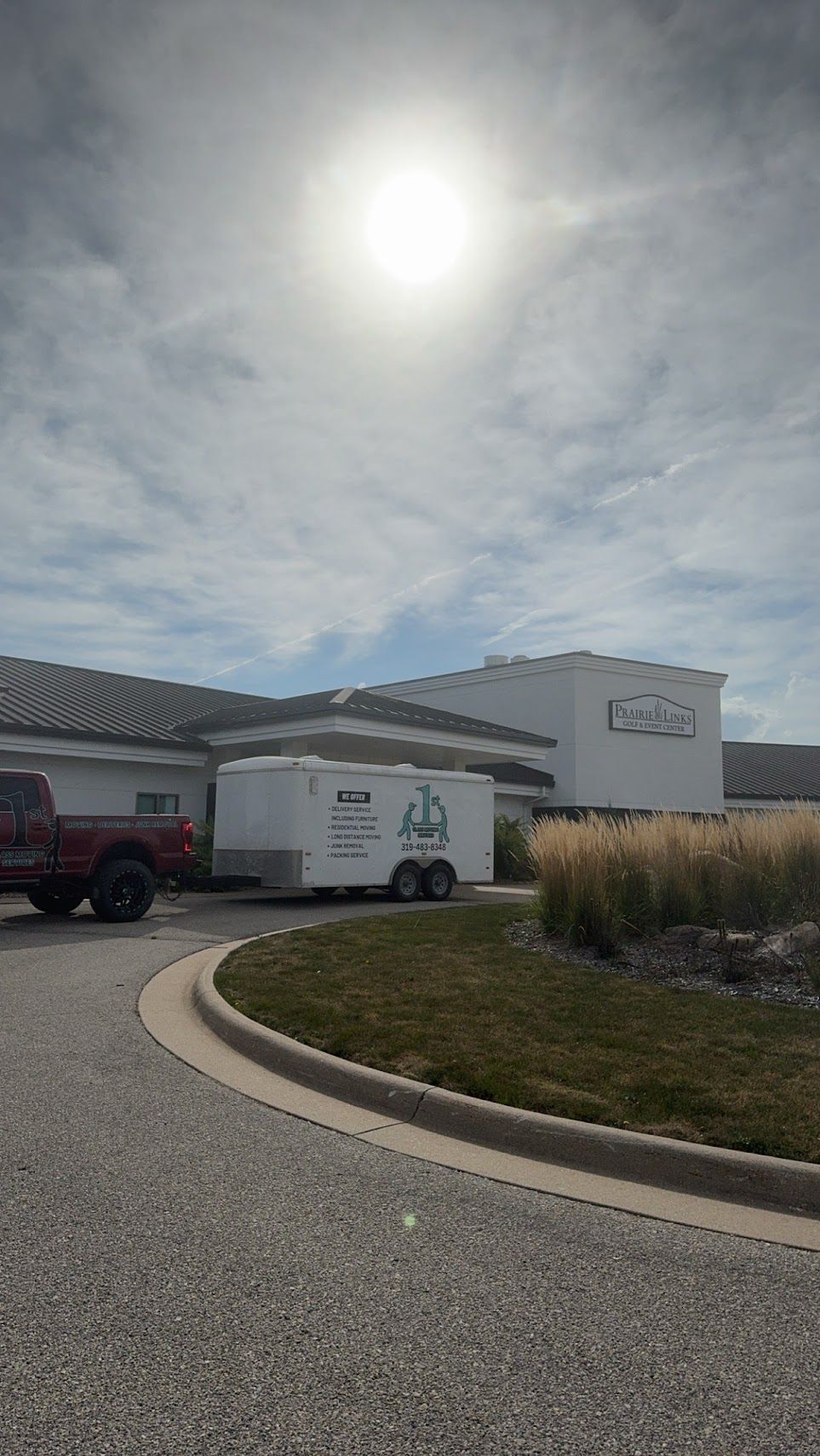 Bright sunny day at a white building with a trailer and a red truck parked outside.