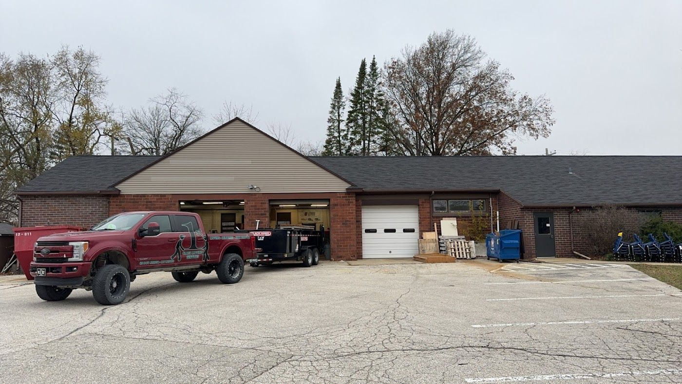 Red truck towing a trailer parked in front of a brick building with open garage doors; overcast day.