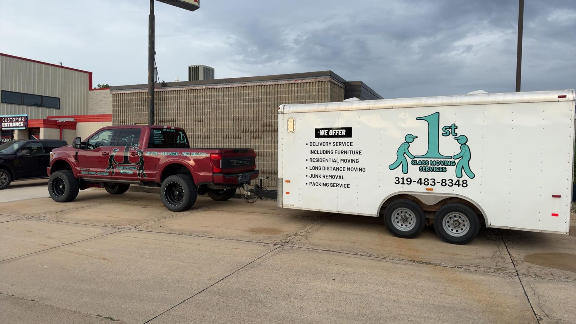 A red pickup truck pulling a white trailer with a logo in a parking lot on a cloudy day.