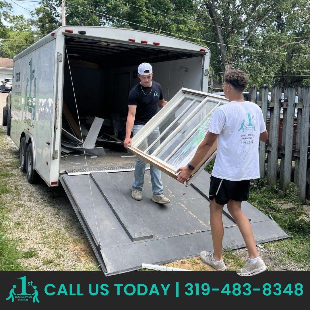 Two men loading a window into a trailer. One wears a black shirt and the other a white shirt, outdoors.