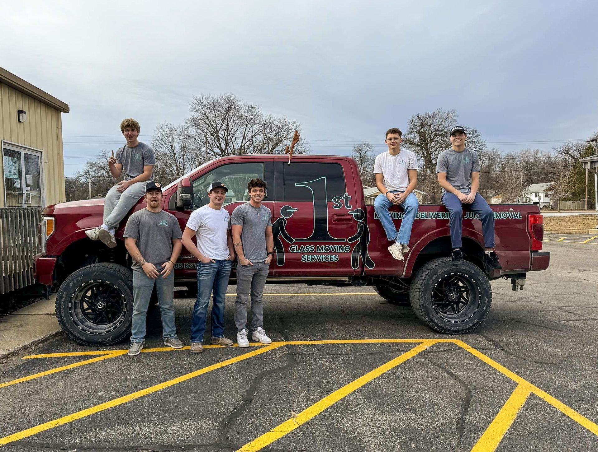 Group of young men pose around a red lifted truck parked in a parking lot.