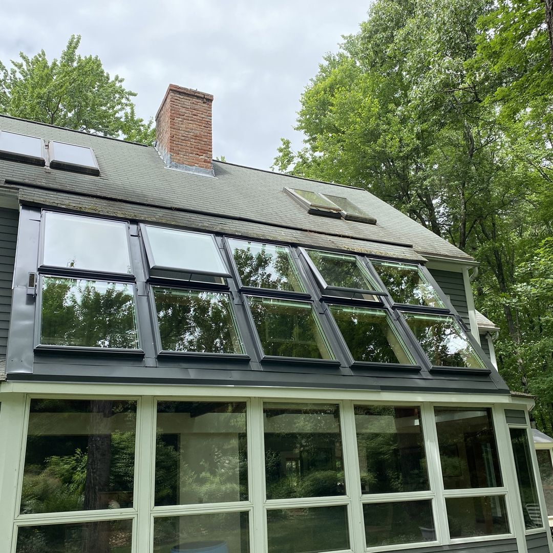 Modern house exterior with large glass windows and a green metal roof surrounded by trees
