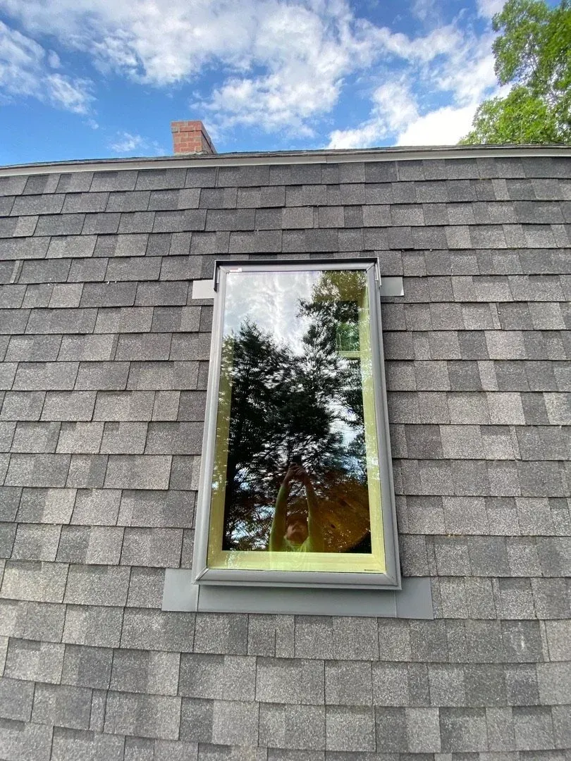 Gray shingled roof with a small skylight reflecting trees and sky