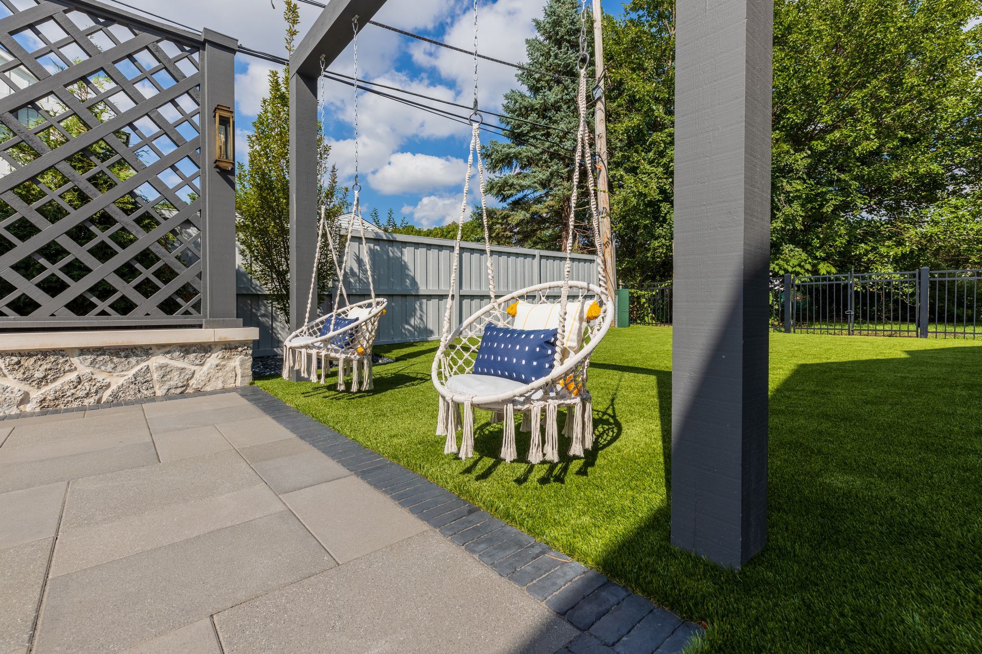 A patio with a pergola and chairs in a backyard.