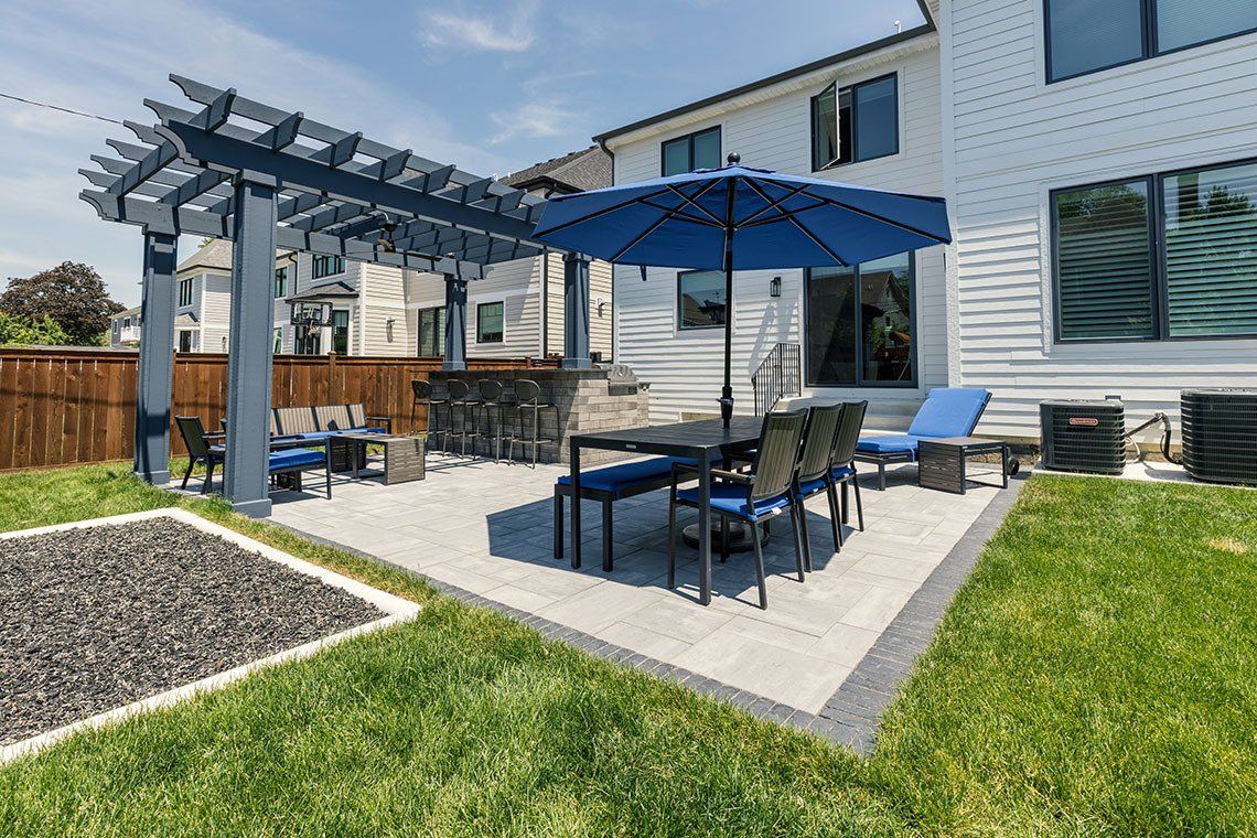 There is a patio with a table and chairs and an umbrella in the backyard of a house.