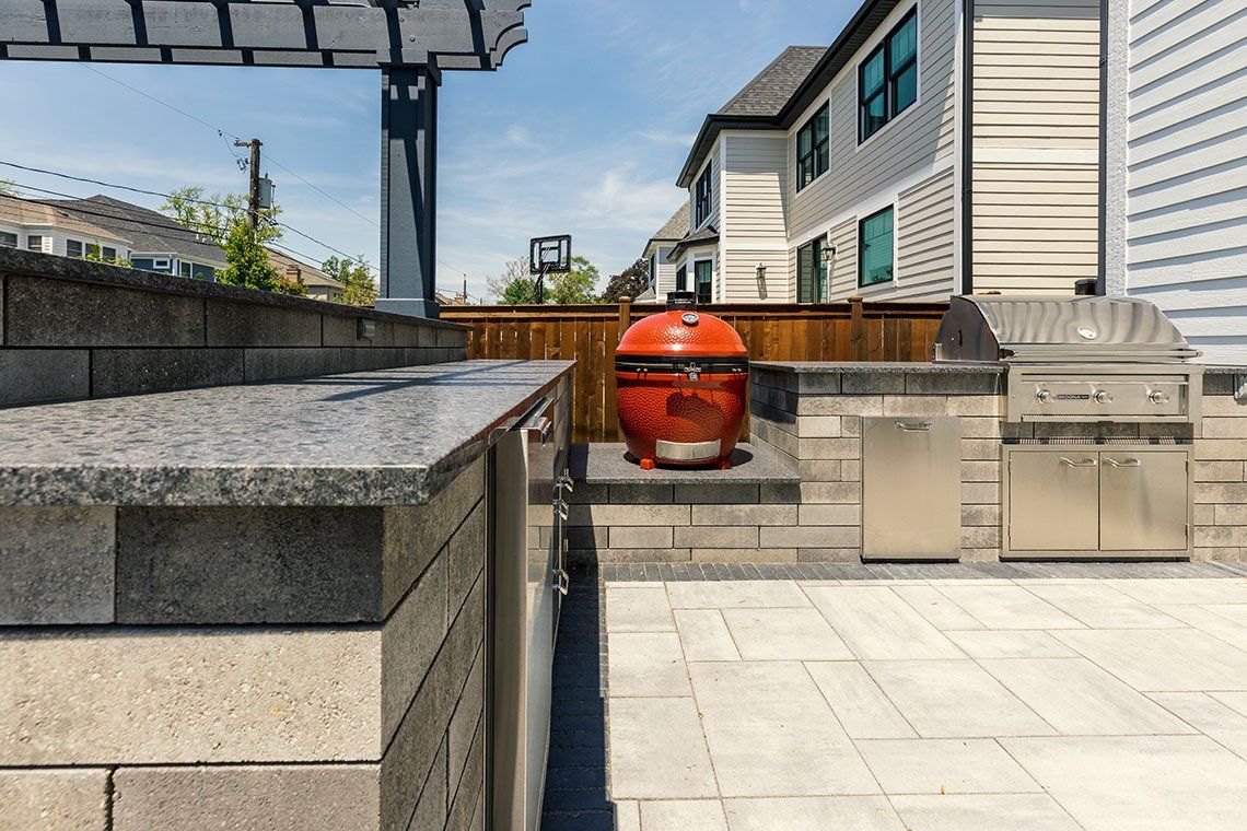 An outdoor kitchen with a grill and a basketball hoop in the background.