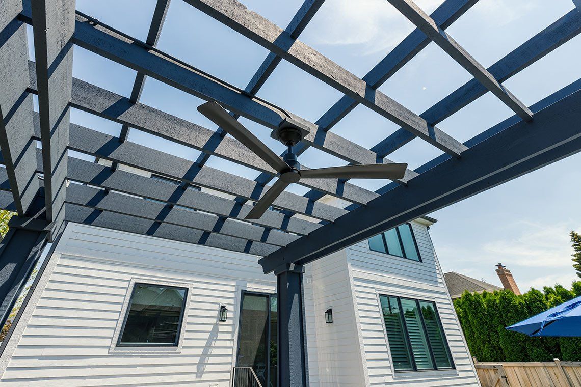 A white house with a blue pergola and a ceiling fan.