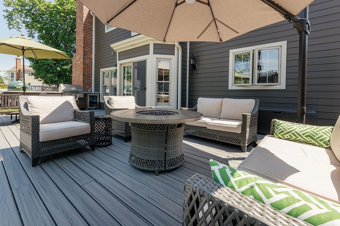 A deck with a couch , chairs , umbrellas and a fire pit.
