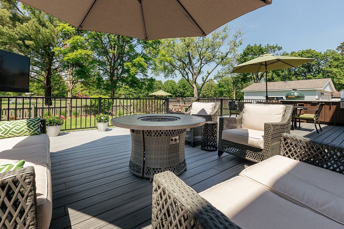 A deck with a fire pit , chairs , umbrellas and a couch.