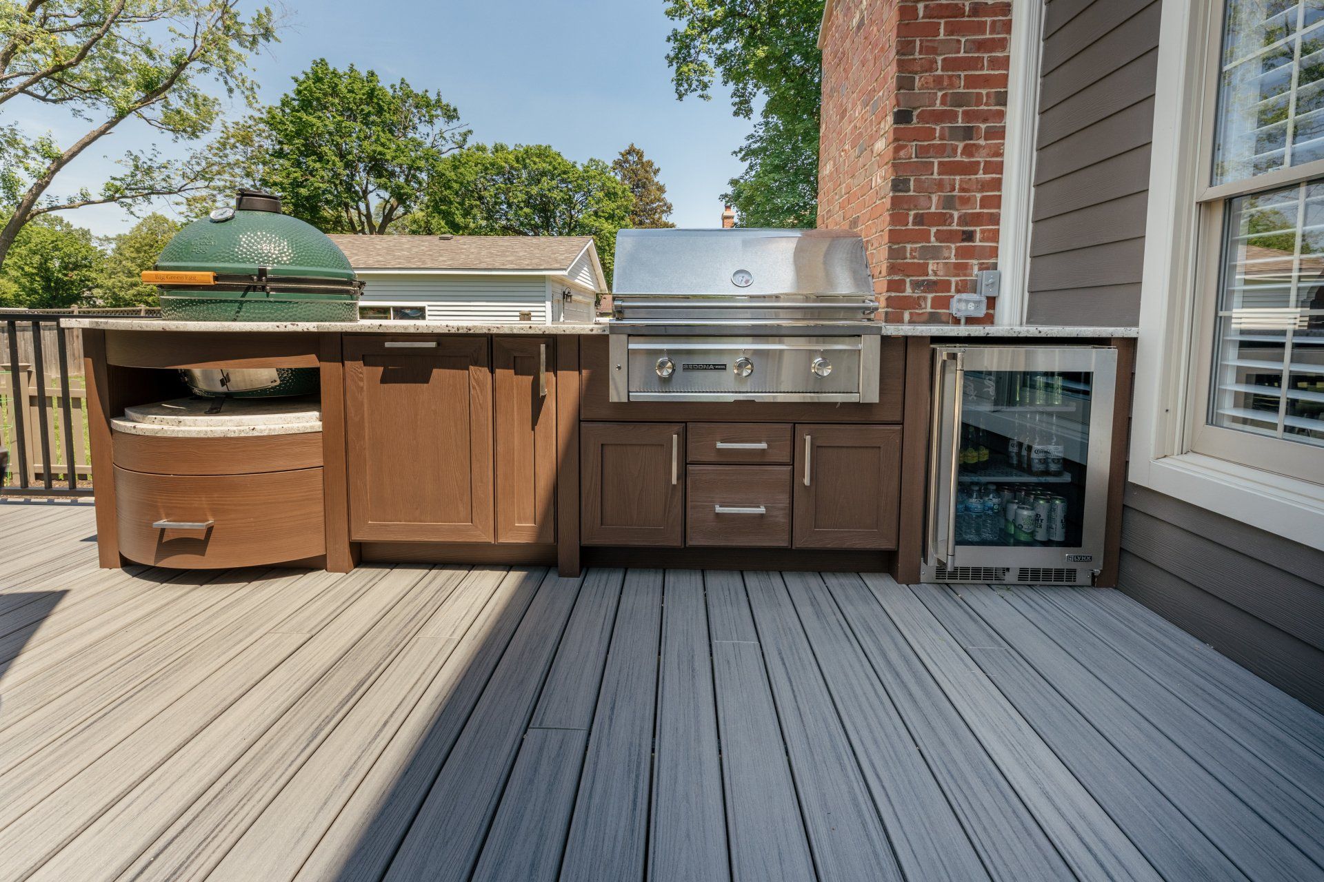 An outdoor kitchen with a grill and a refrigerator on a deck.