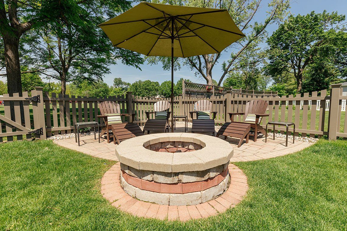 There is a fire pit in the middle of the yard with a yellow umbrella.