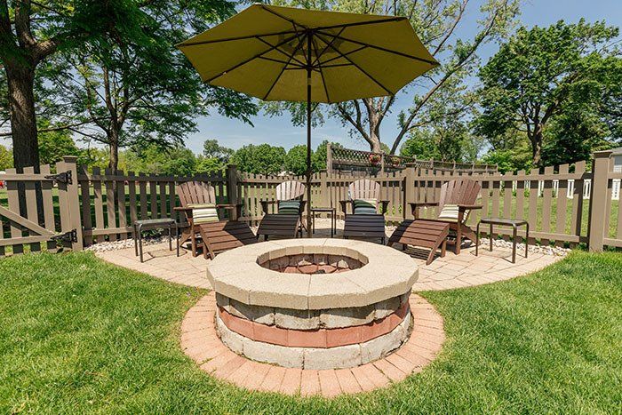 There is a fire pit in the middle of the yard with a yellow umbrella.