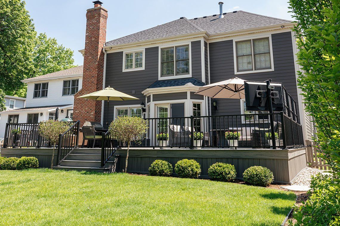 A large house with a large deck and umbrellas in the backyard.