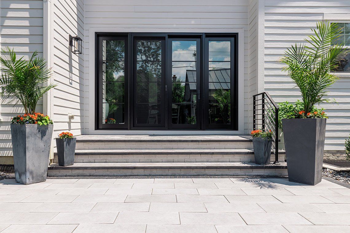 A white house with black sliding glass doors and planters in front of it.