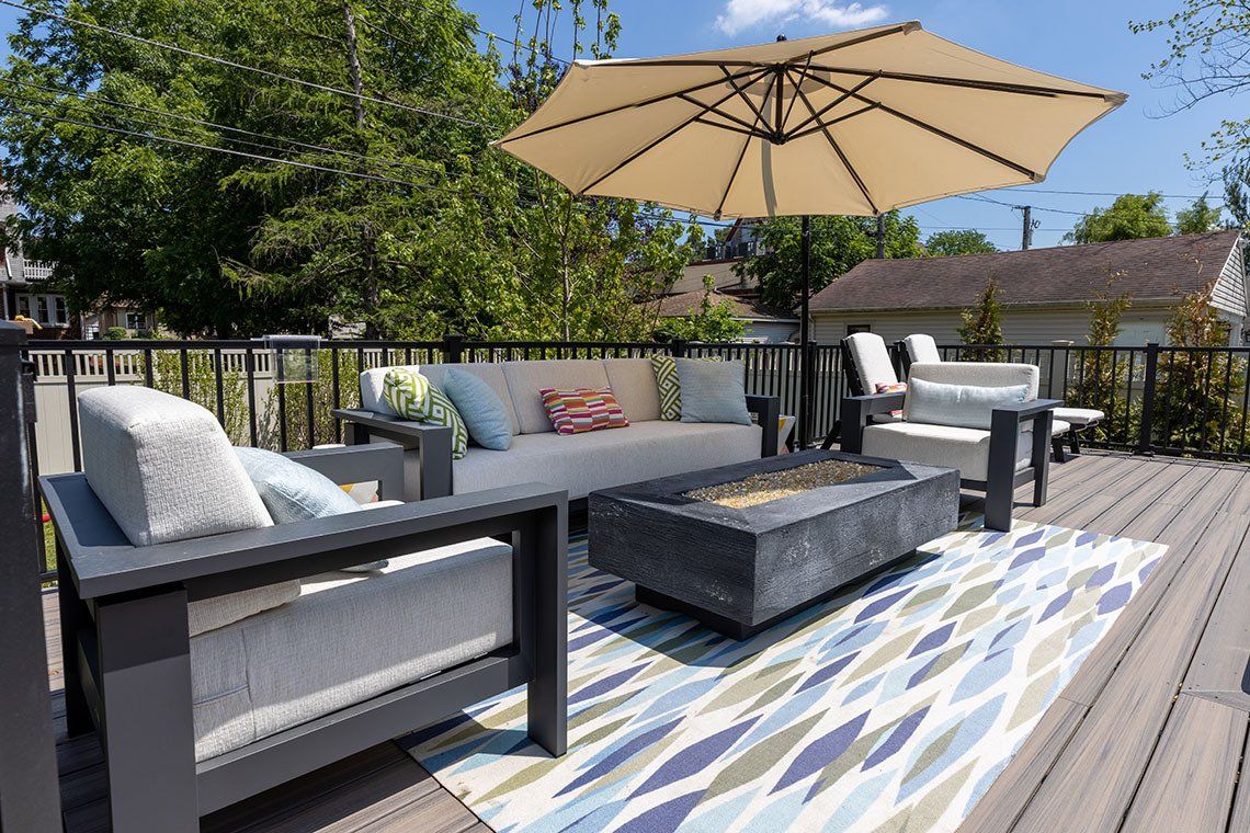 A deck with a couch , chairs , coffee table and umbrella.