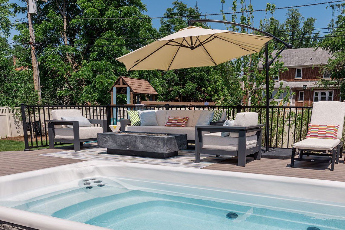 A swimming pool with a couch , chairs , and an umbrella on the deck.