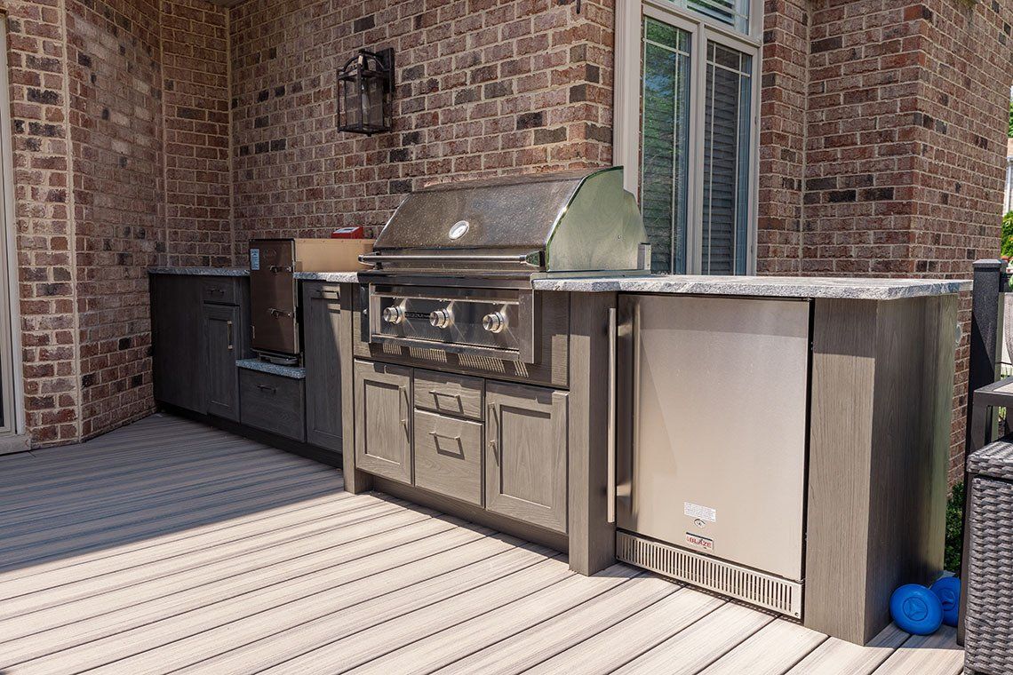 An outdoor kitchen with a grill and a refrigerator on a deck.