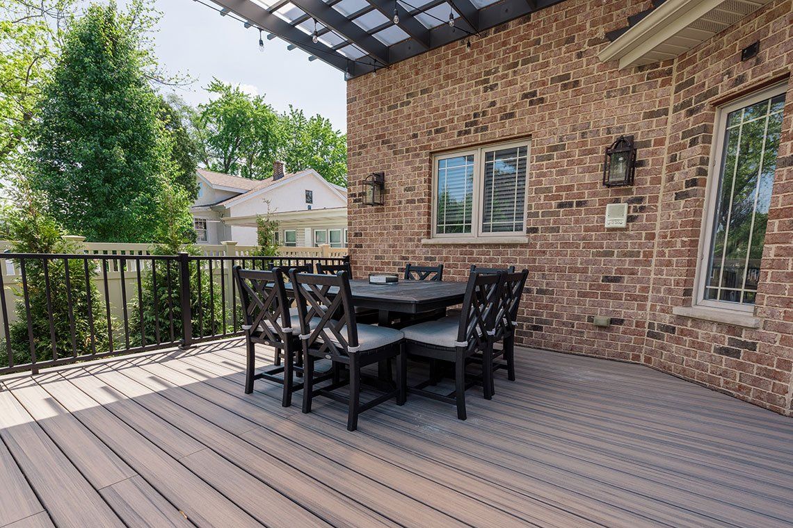 There is a table and chairs on the deck of a brick house.