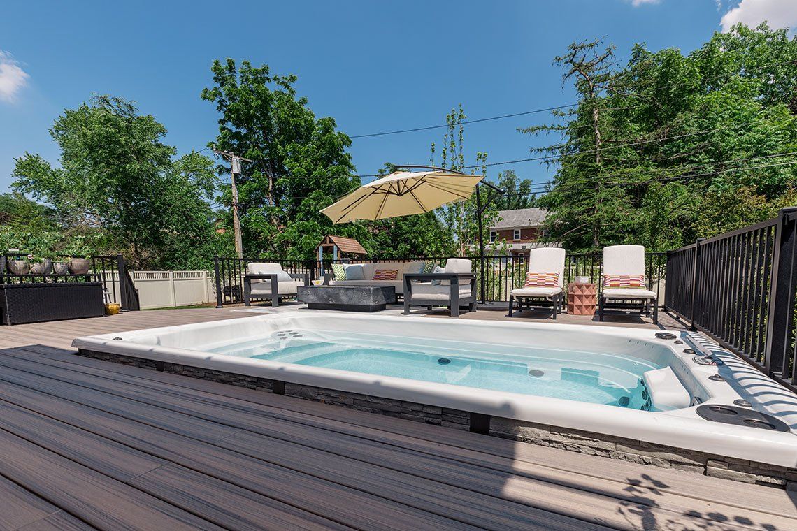 A hot tub is sitting on top of a wooden deck next to a fence.