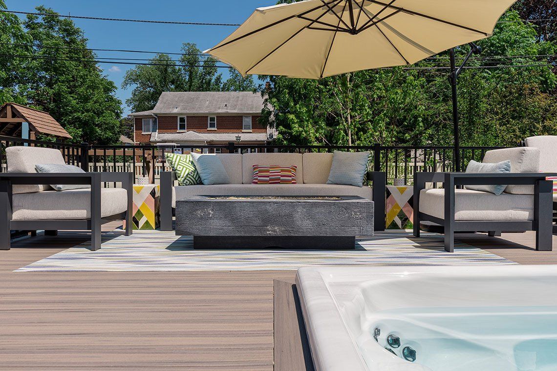 A patio with a couch , chairs , umbrella and a hot tub.
