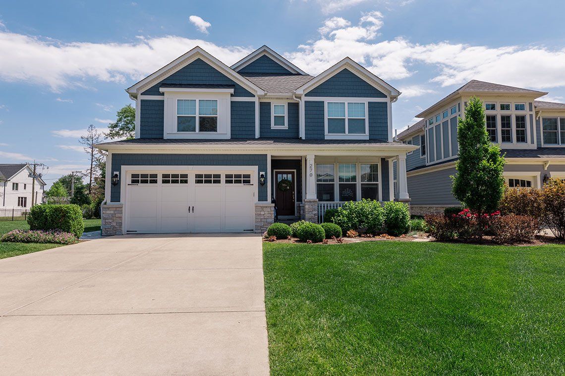 A large blue house with a white garage door is sitting on top of a lush green lawn.