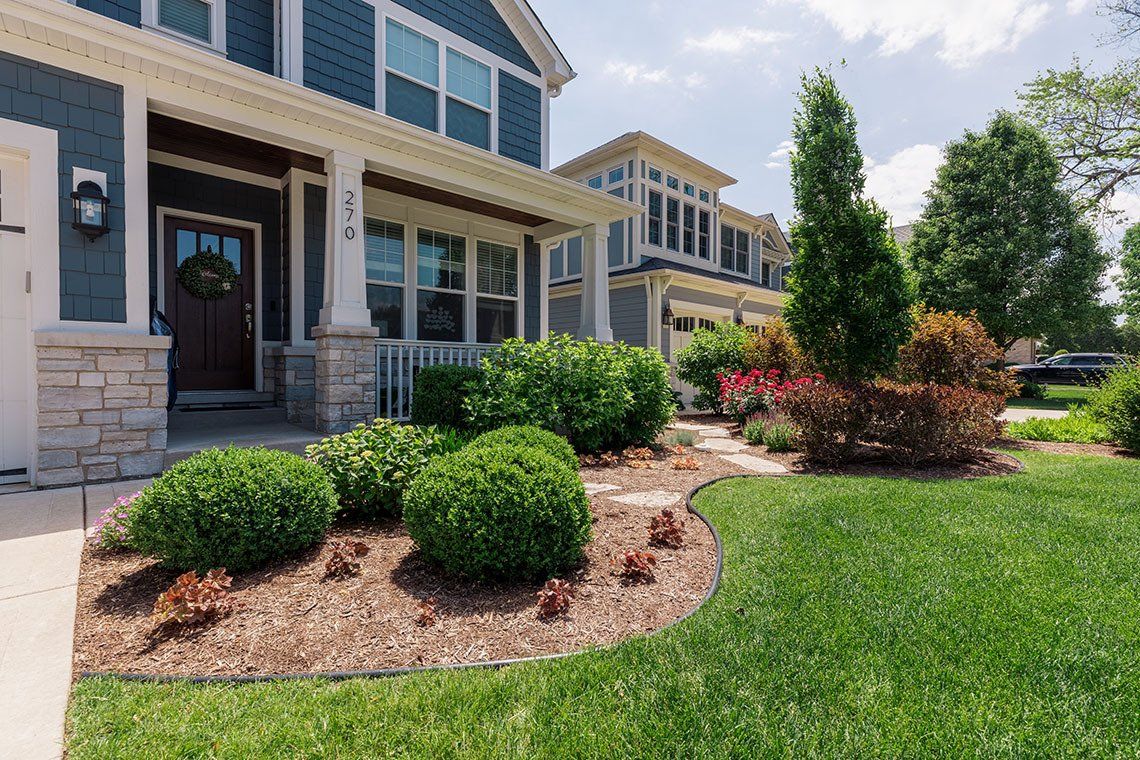 A house with a lush green lawn and bushes in front of it.