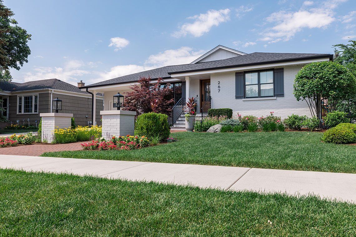 A white house with a lush green lawn and a sidewalk in front of it.