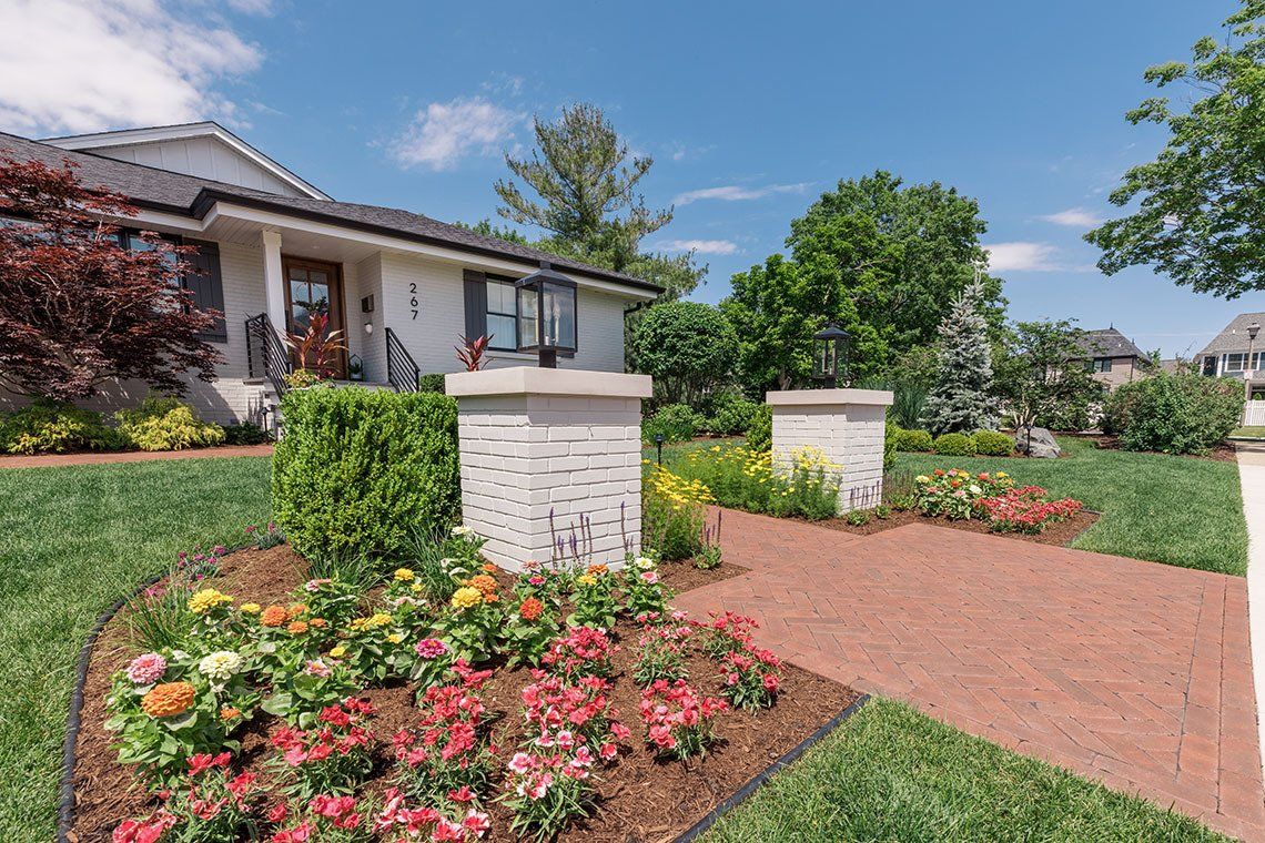 A white house with a brick walkway and flowers in front of it.