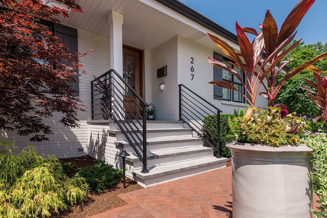 The front of a white brick house with stairs and a potted plant in front of it.
