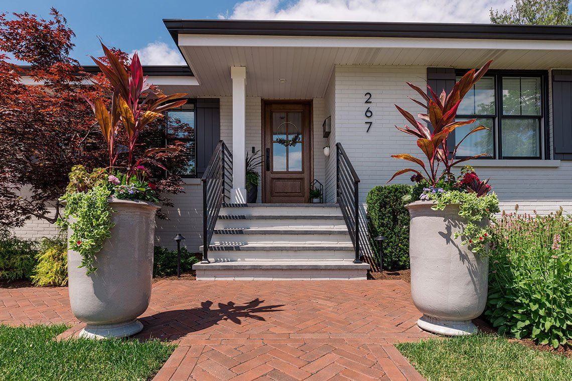 A white house with a brick walkway and planters in front of it.
