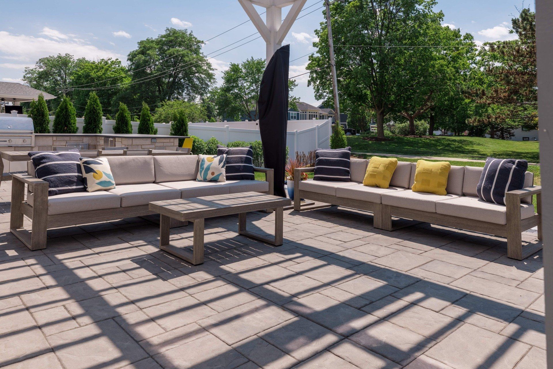 A patio with a couch , table , and umbrella under a pergola.