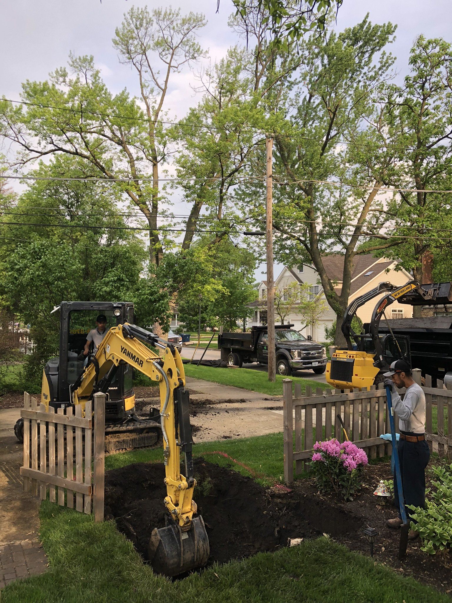 A yellow excavator is digging a hole in a yard.