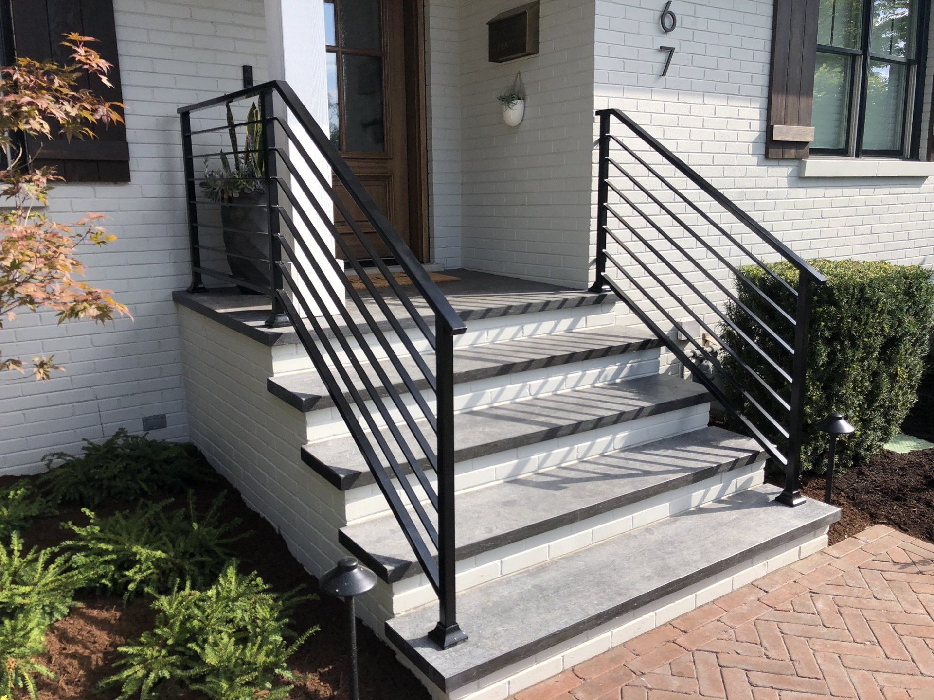A white brick house with a black railing and stairs