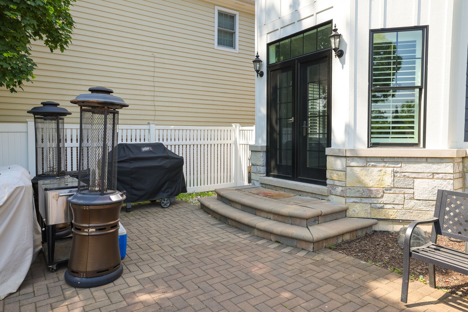 A patio with a grill and heaters in front of a house.