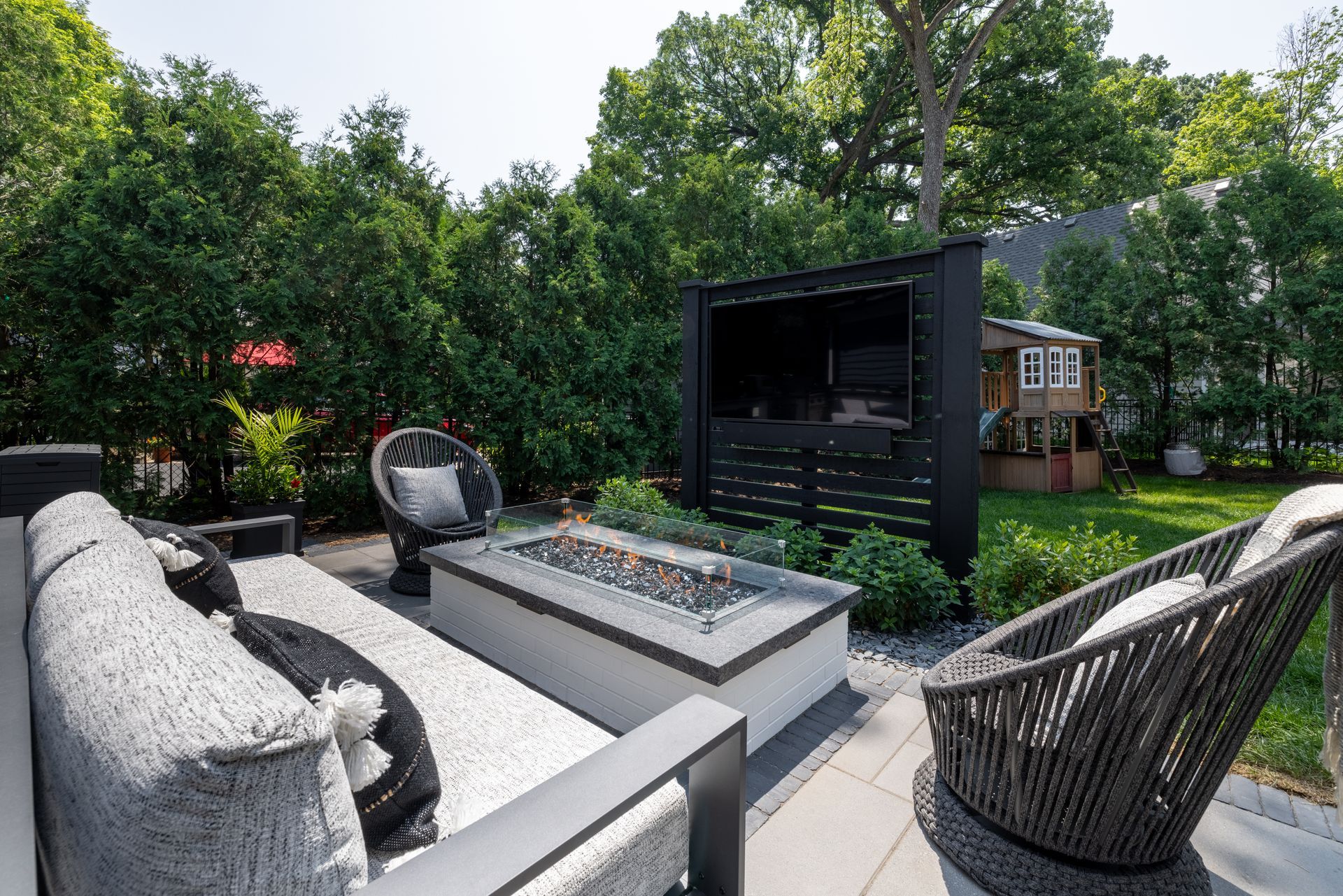 A patio with a fire pit , couch , chairs and a television.