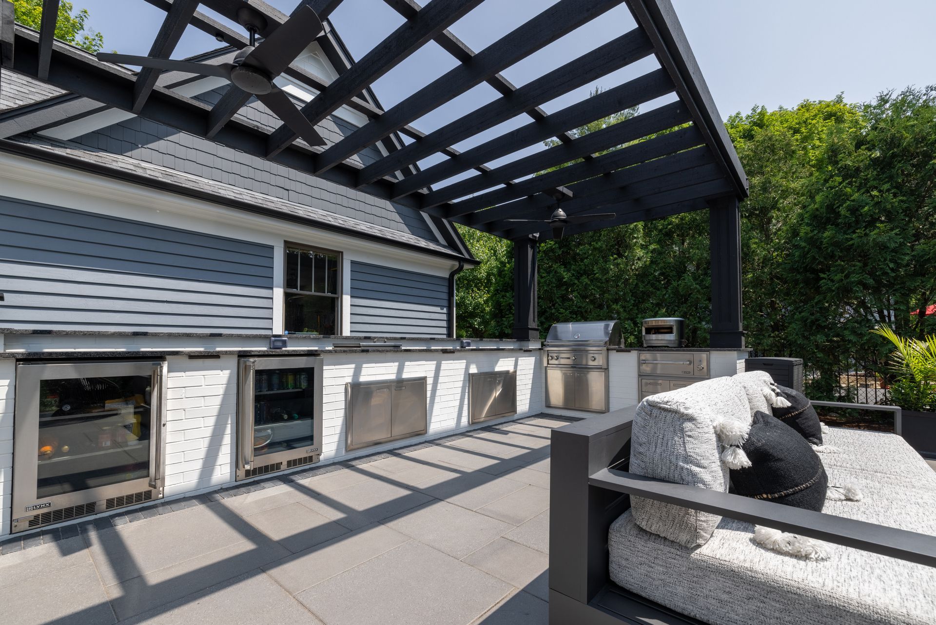A patio with a couch and a grill under a pergola.