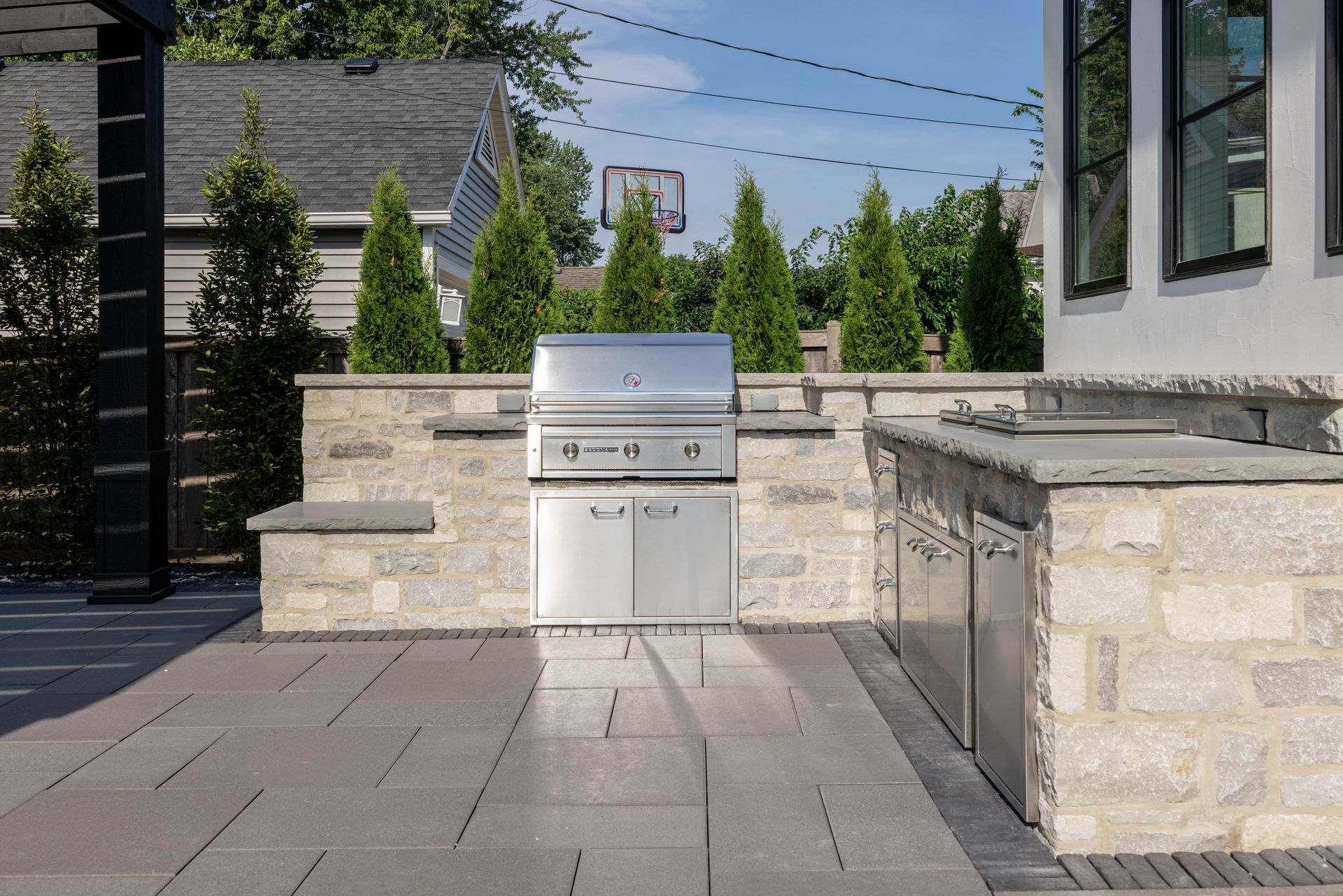 A stainless steel grill is sitting on a patio next to a stone wall.