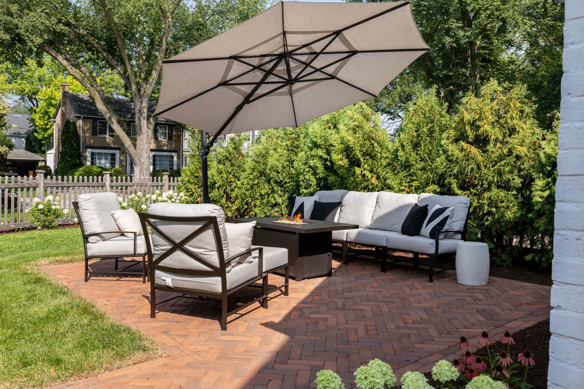 A patio with a couch , chairs , umbrella and fire pit.