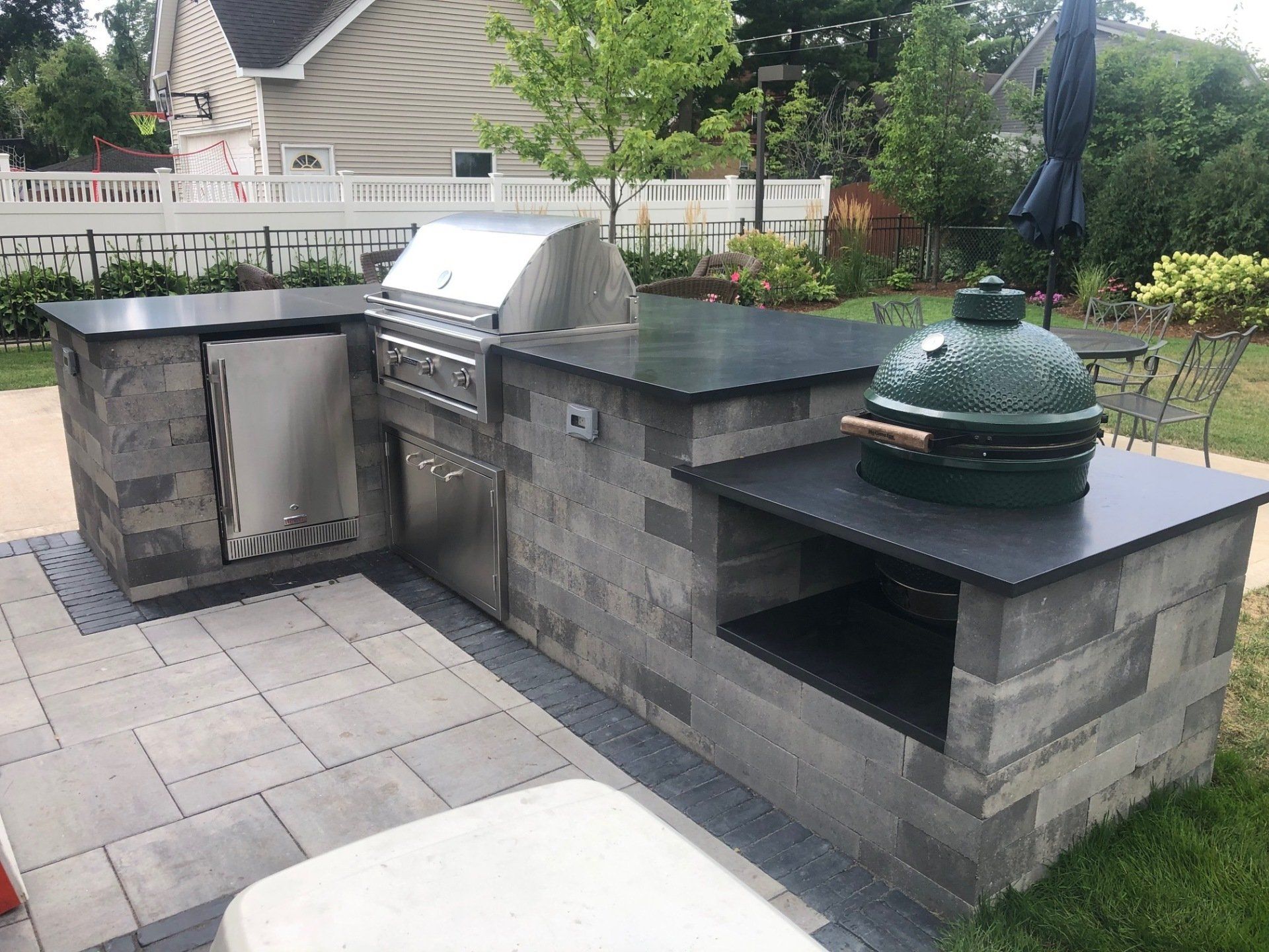 A large green egg grill is sitting on top of a brick counter in a backyard.