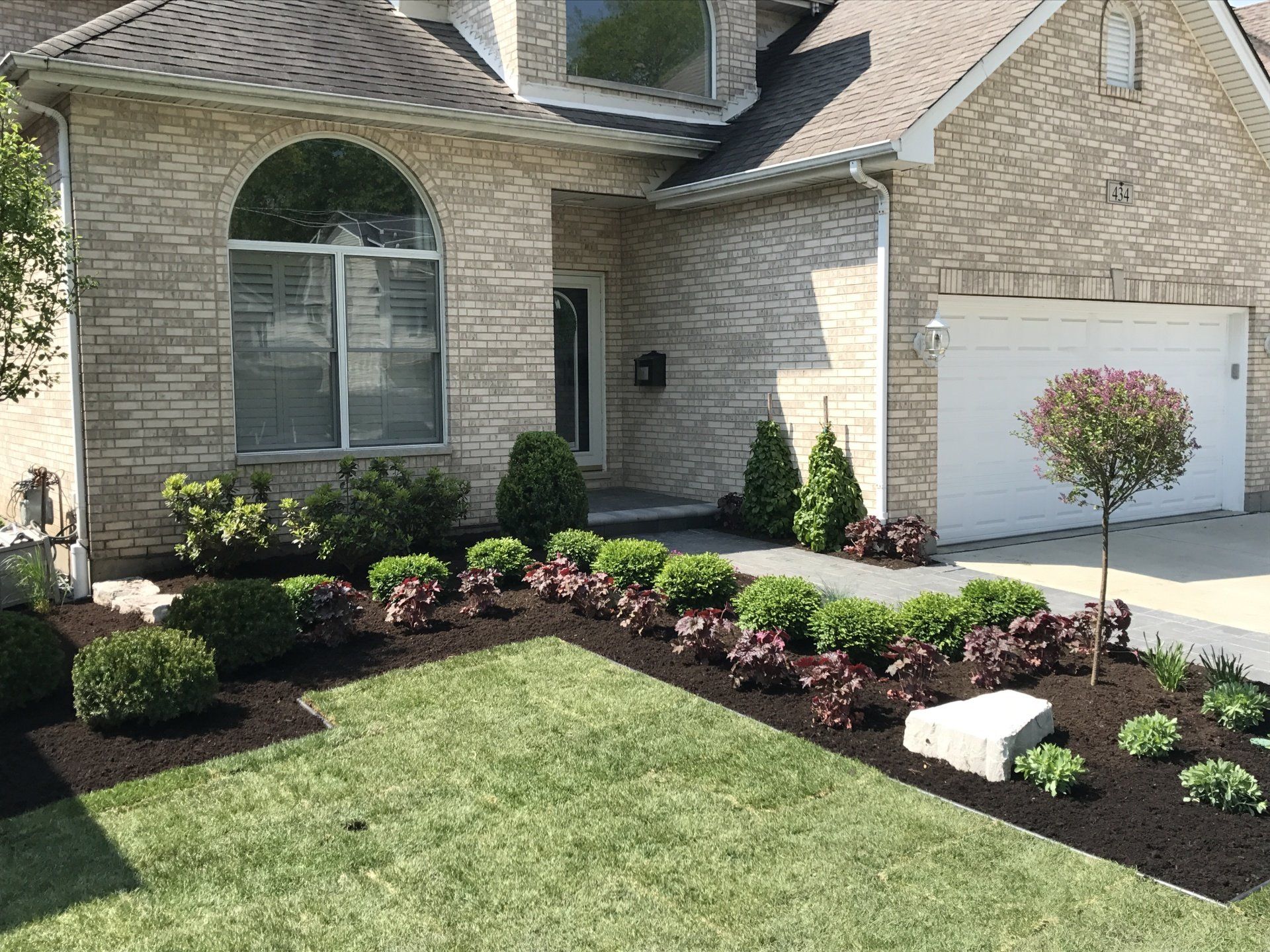 A brick house with a white garage door and a lush green lawn in front of it.