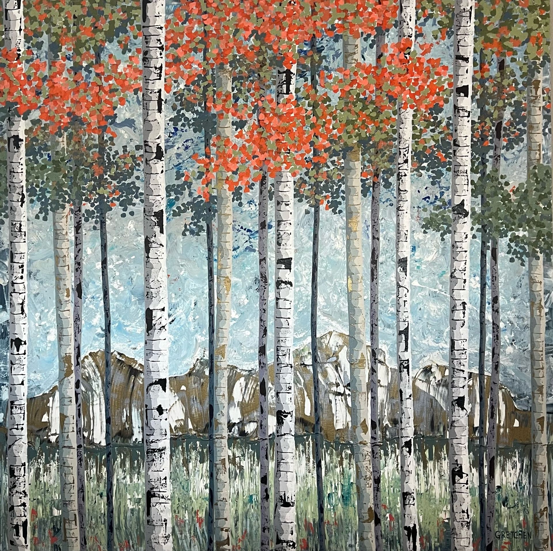 Aspen trees with red and green leaves frame a view of mountains reflecting in the water.