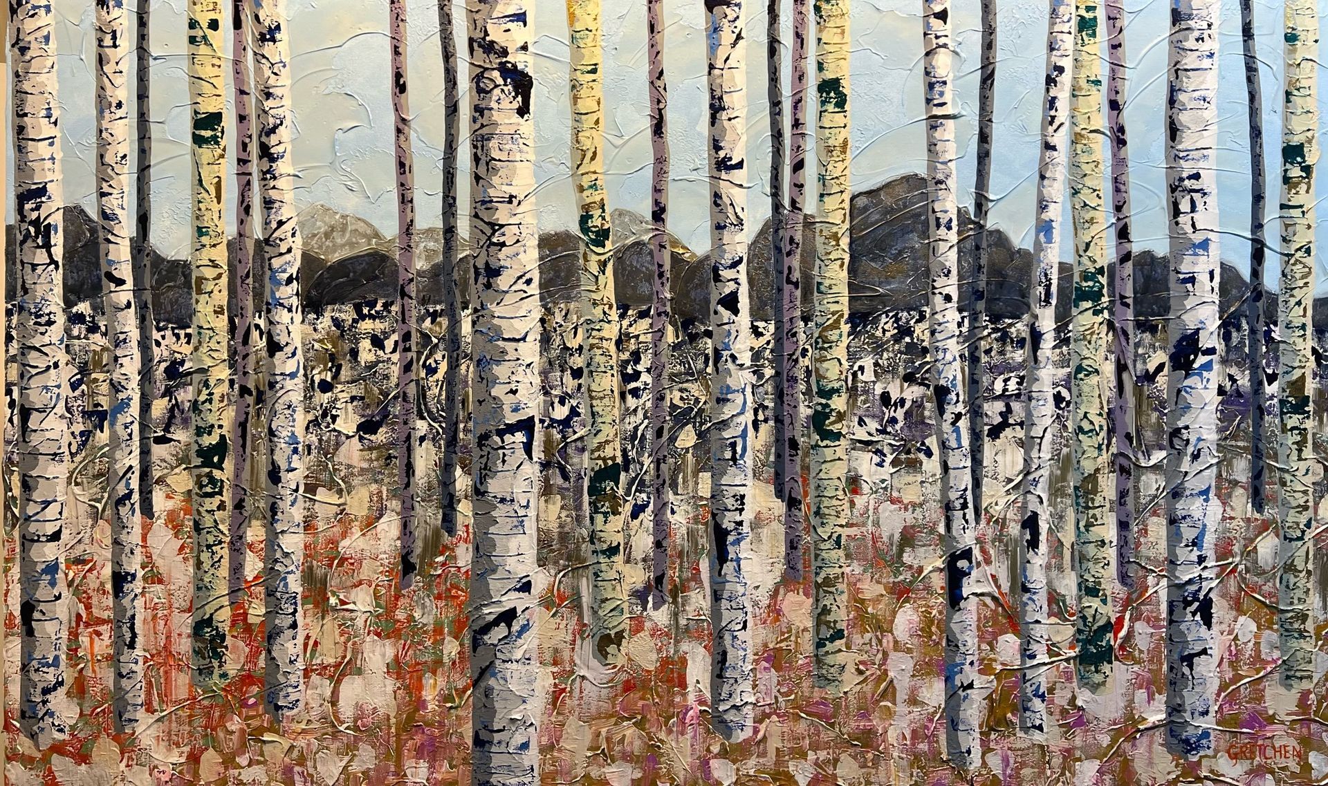 Birch trees in a forest with brown and white bark. Mountains in the background.