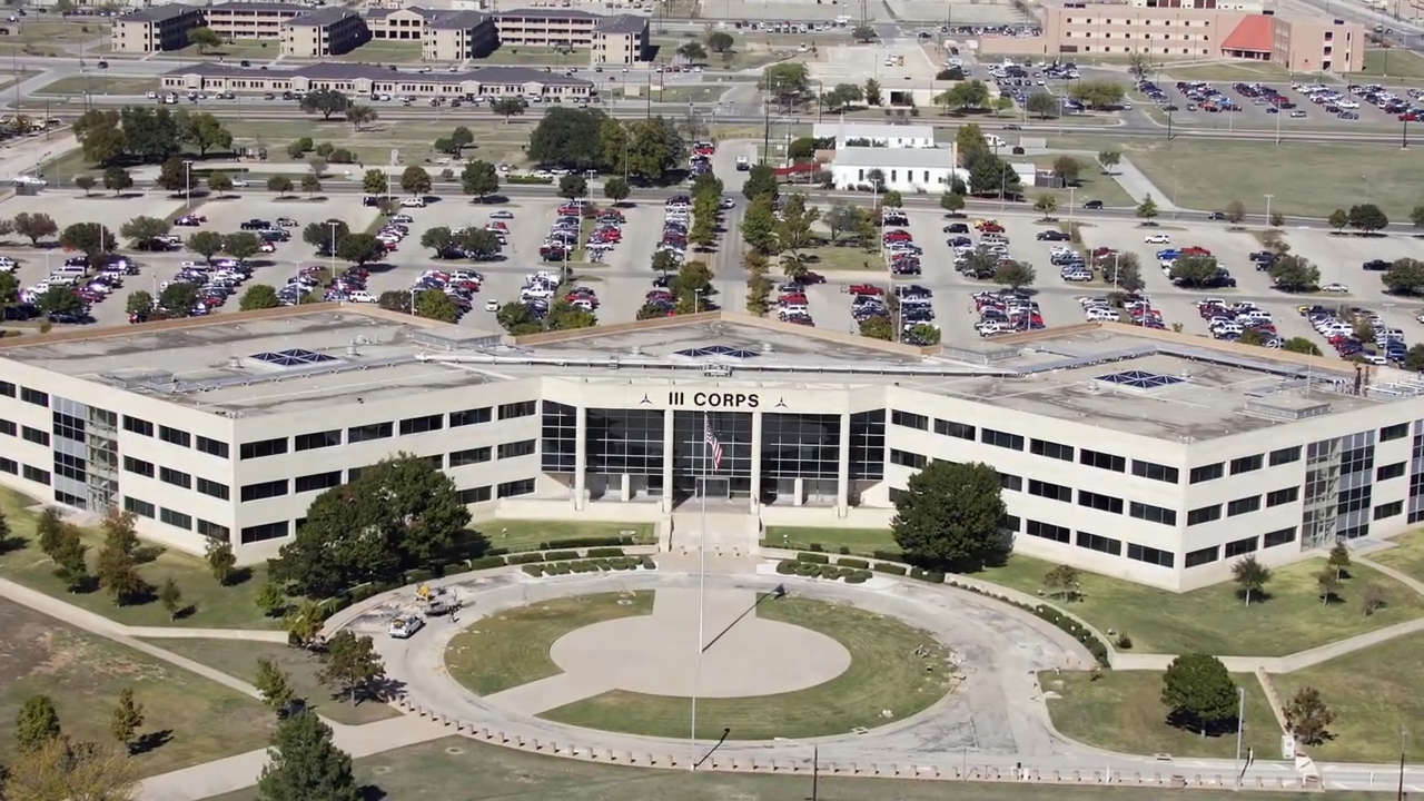 An aerial view of the light-colored, multi-story E-Dorm building at Fort Leonard Wood, surrounded by parking and lawns.